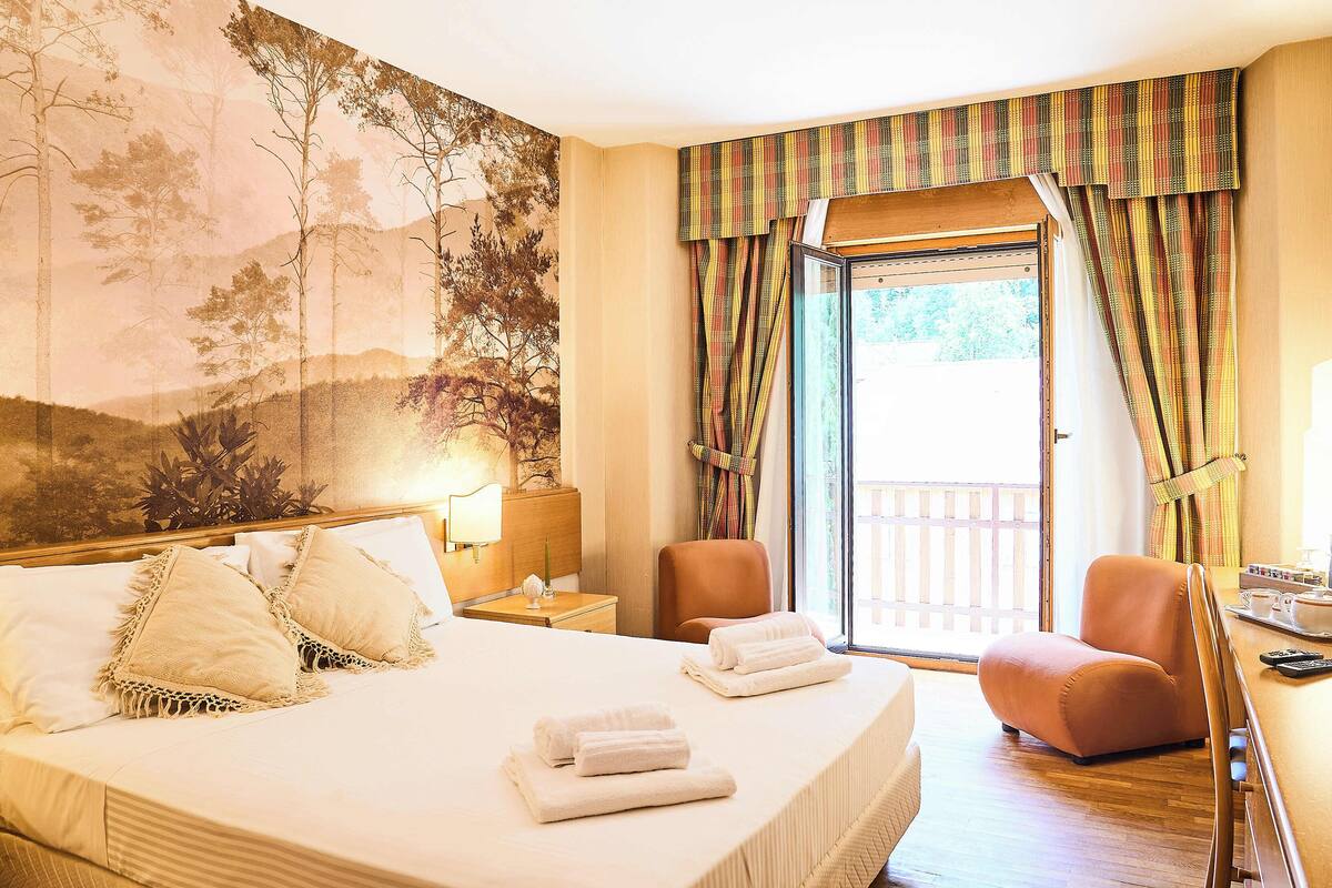 A hotel room with a large bed, a desk, a chair, and a view of the outdoors.