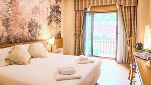 A hotel room with a large bed, a wooden headboard, a nightstand with a lamp, and a view of the outside through a sliding glass door. - Hotel Camigliatello (Spezzano della Sila)