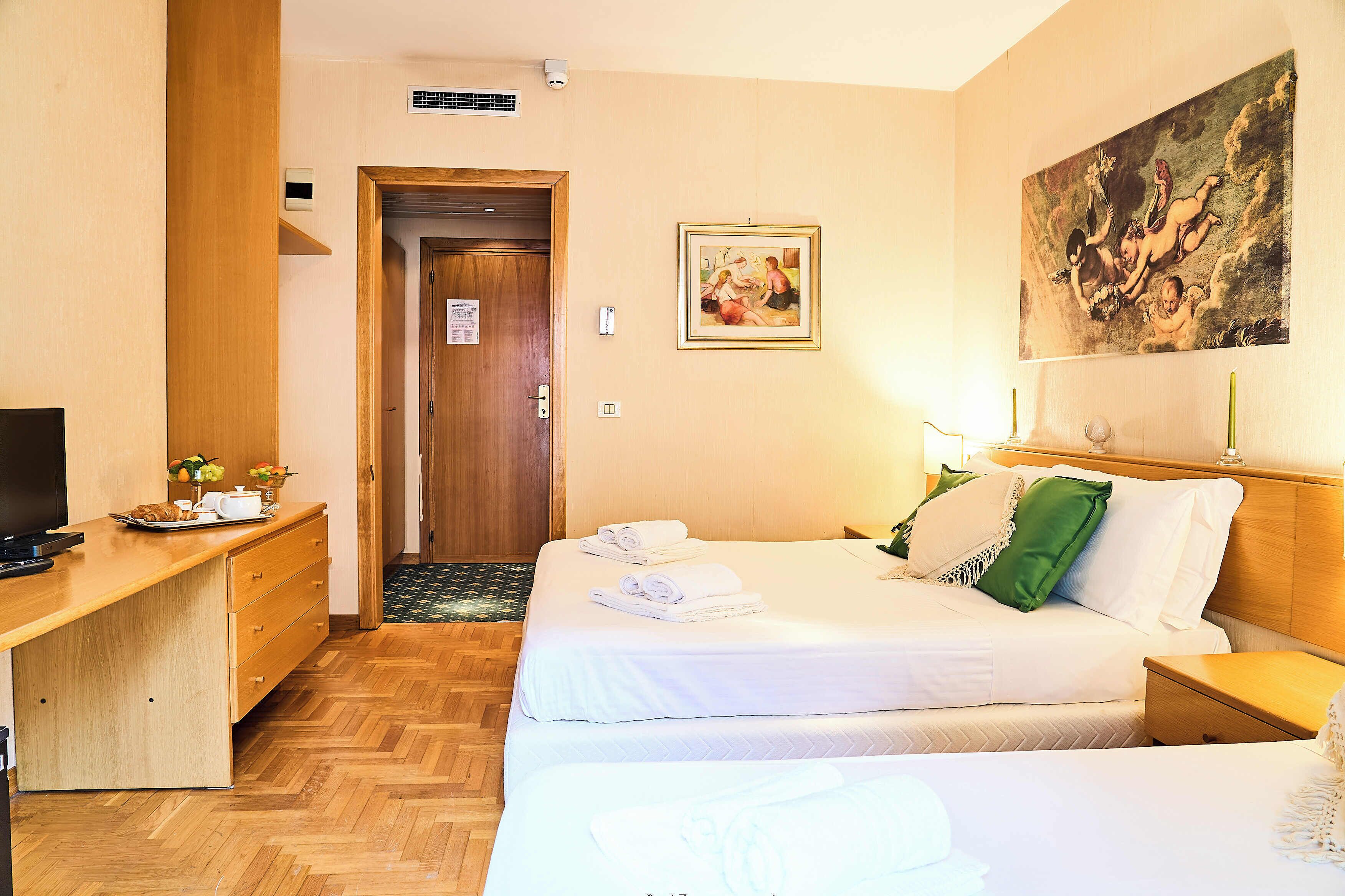 Habitación de hotel con dos camas, un escritorio, un televisor y un cuadro en la pared.