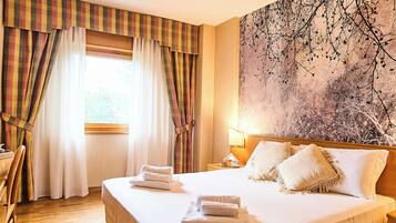 A hotel room with a large bed, two pillows, a nightstand with a lamp, and a window with curtains.