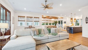 A spacious living room with a large sectional sofa, a wooden coffee table, and a ceiling fan. - Beach Access Directly Across Street! Ocean view, Private Pool, Hot Tub, Luxe New Construction (Isle Of Palms)