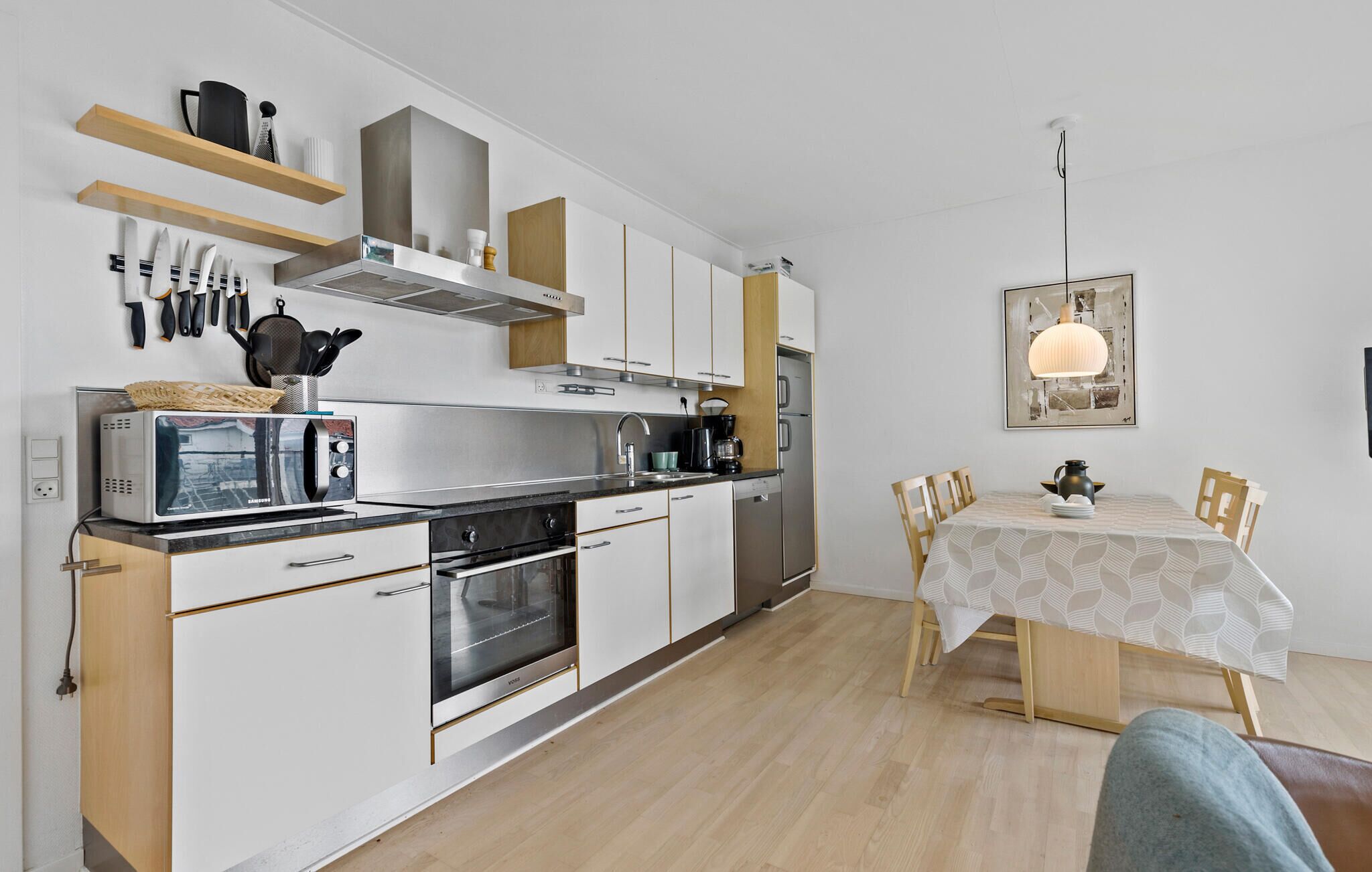 A modern kitchen with white cabinets, a built-in oven, and a dining area with a table and chairs.