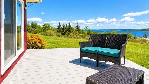 A deck with a wicker sofa and ottoman, overlooking a lake and greenery.