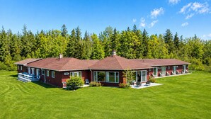 A two-story house with a red exterior, large windows, and a well-maintained lawn.