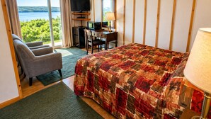 A hotel room with a large bed, a desk with a computer, a television, and a view of the outdoors.