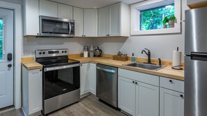 Uma cozinha moderna com armários brancos, eletrodomésticos de aço inoxidável, bancada de madeira e janela com vista para o verde.