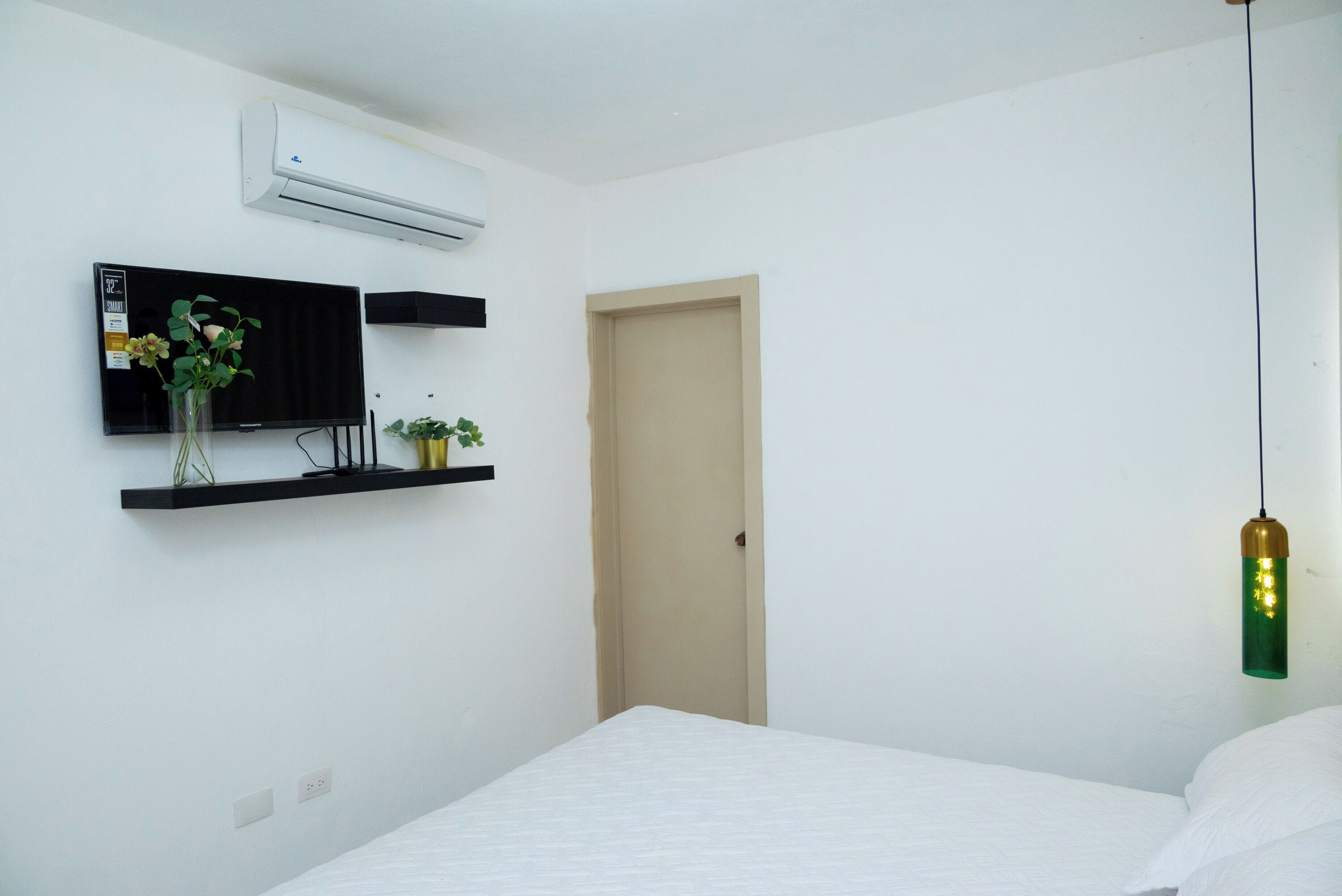 Et soveværelse med seng, ophængt fjernsyn, fastgjort aircondition og en pendel.