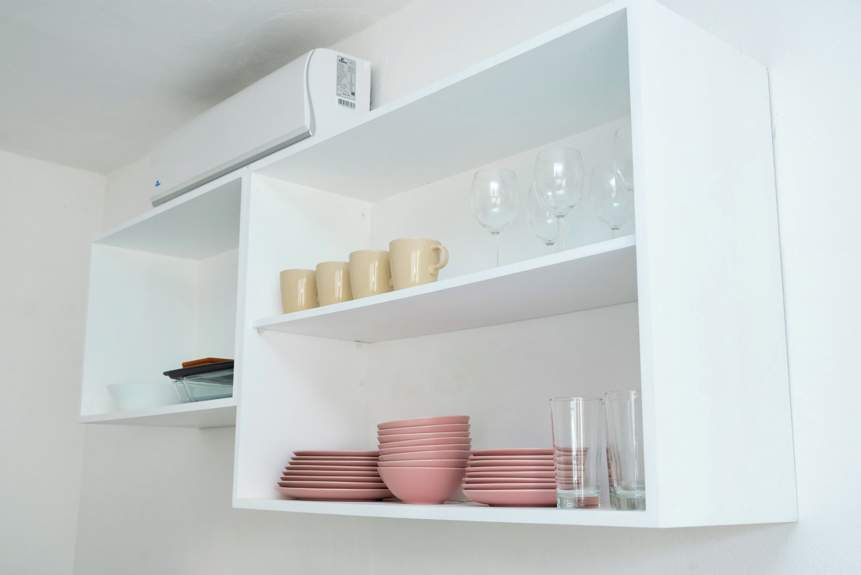 A white shelf with stacked pink bowls and glasses.