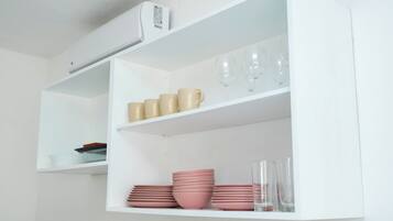 A white shelf with stacked pink bowls and glasses.
