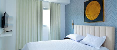 Habitación de hotel con cama, cortinas, televisor montado en la pared y un adorno decorativo.