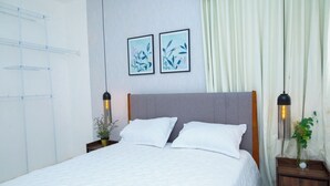 A neatly made bed with white linens, a grey headboard, and two bedside tables with lamps. There are two framed artworks on the wall above the bed. - Apartahotel Señorial (Higuey)