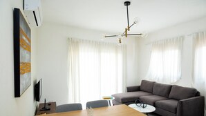 A modern living room with a wooden dining table, grey sofa, and a small white table with a lamp. - Apartahotel Señorial (Higuey)