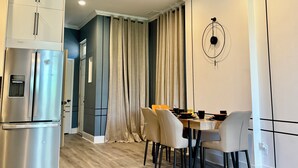 Una cocina moderna con refrigerador integrado, un comedor con mesa y sillas, y un amplio ventanal con cortinas.