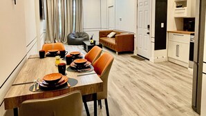 Een moderne keuken met witte kasten, een zwarte koelkast en een eethoek met een houten tafel en oranje stoelen.