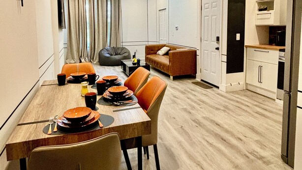 Una cocina moderna con armarios blancos, un refrigerador negro y una zona de comedor con una mesa de madera y sillas naranjas.