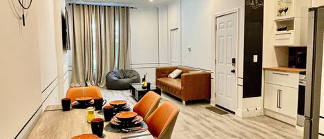 Une cuisine moderne avec des meubles blancs, un réfrigérateur noir et un coin repas comprenant une table en bois et des chaises orange.