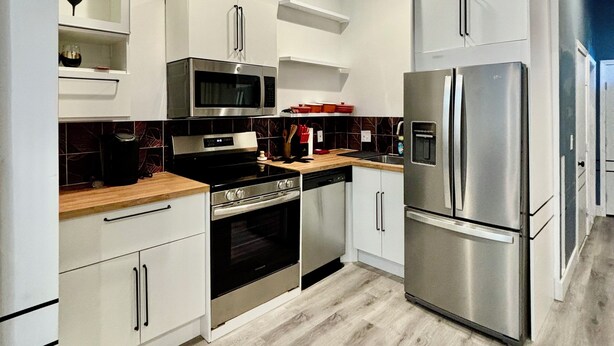 Een moderne keuken met witte kasten, roestvrijstalen apparatuur en een houten aanrecht.
