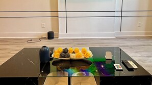 Een moderne woonkamer met een grote flatscreen televisie aan de muur, een glazen salontafel met decoratieve objecten en een paar houten manden.