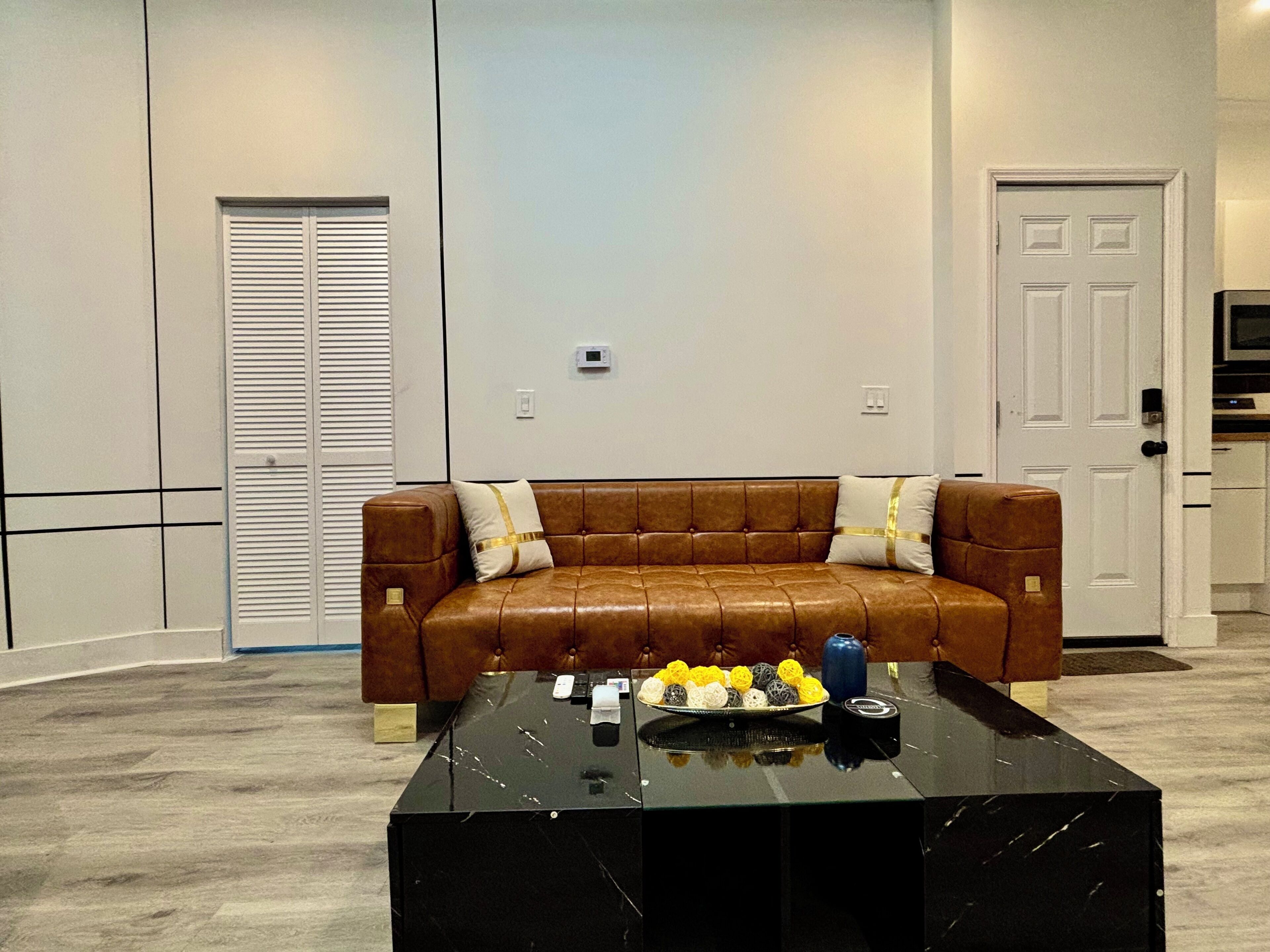A living room with a brown leather sofa, a black marble coffee table, and a door in the background.