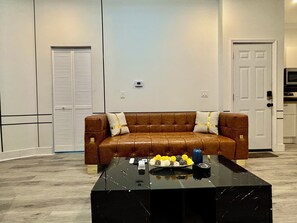 Un salon avec un canapé en cuir marron, une table basse en marbre noir et une porte visible au fond.