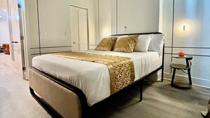 Een moderne slaapkamer met een groot bed, een nachtkastje, een klein krukje en een plafondventilator.