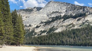 A beach with clear water, a mountain in the background, and a forested area.