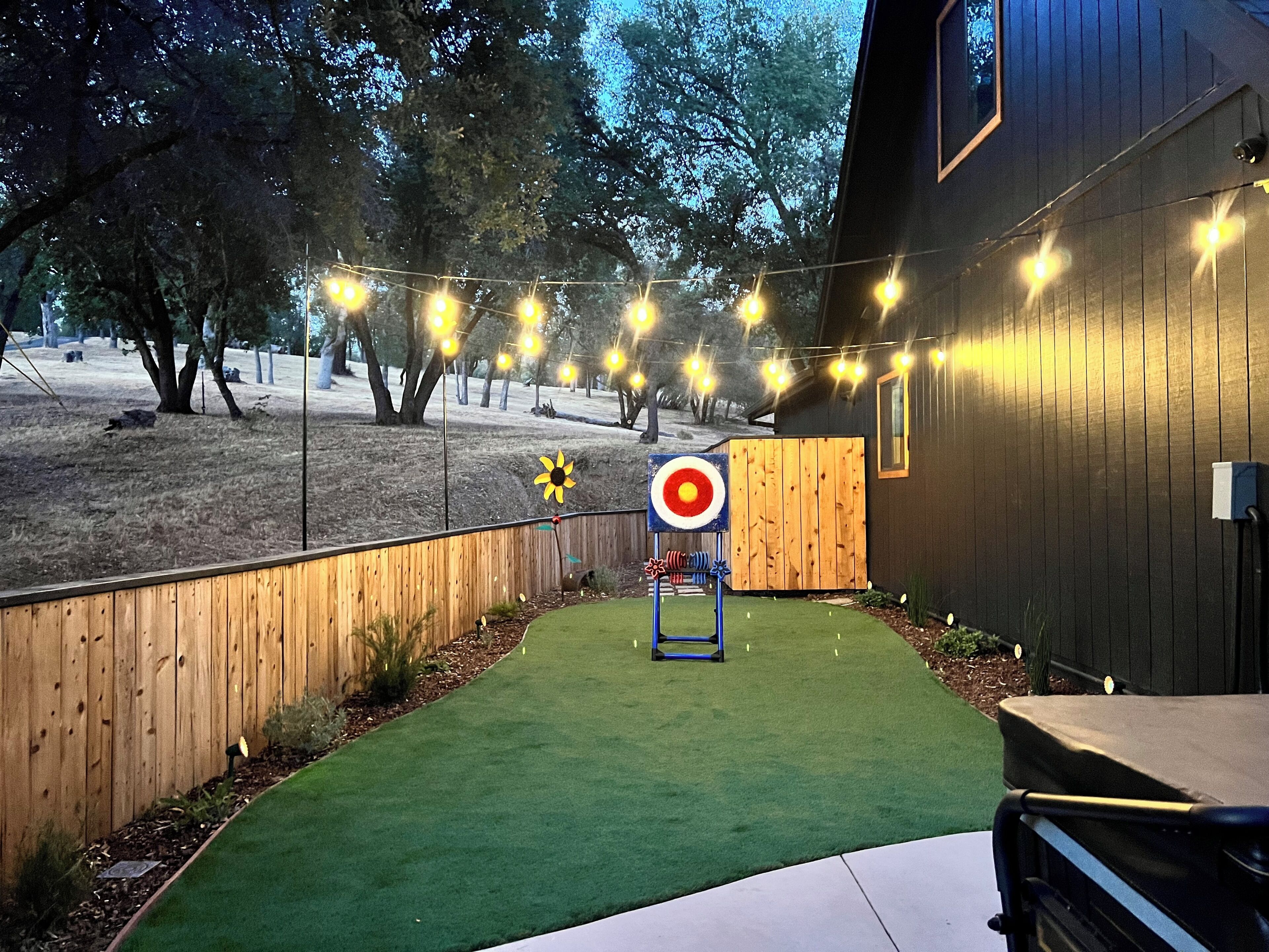 A backyard with artificial grass, a wooden fence, and string lights.
