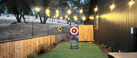 A backyard with artificial grass, a wooden fence, and string lights.