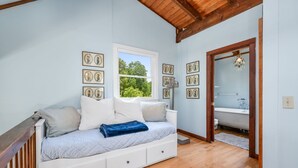 Een slaapkamer met een bed, een raam en een zichtbare badkamer door een geopende deur.