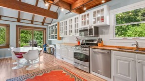 Een moderne keuken met witte kasten, roestvrijstalen apparatuur en een groot raam met uitzicht op groen.