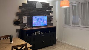 Ein modernes Wohnzimmer mit einem Holzespeisetisch, einem Fernseher auf einer Holzunterhaltungseinheit und einer hängenden, orangefarbenen Pendelleuchte.