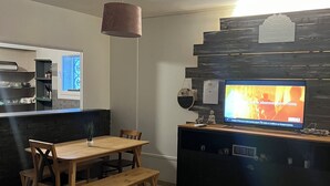 Eine moderne Küche mit Essbereich, einem Fernseher auf einem schwarzen Schrank und einer hängenden Pendelleuchte.