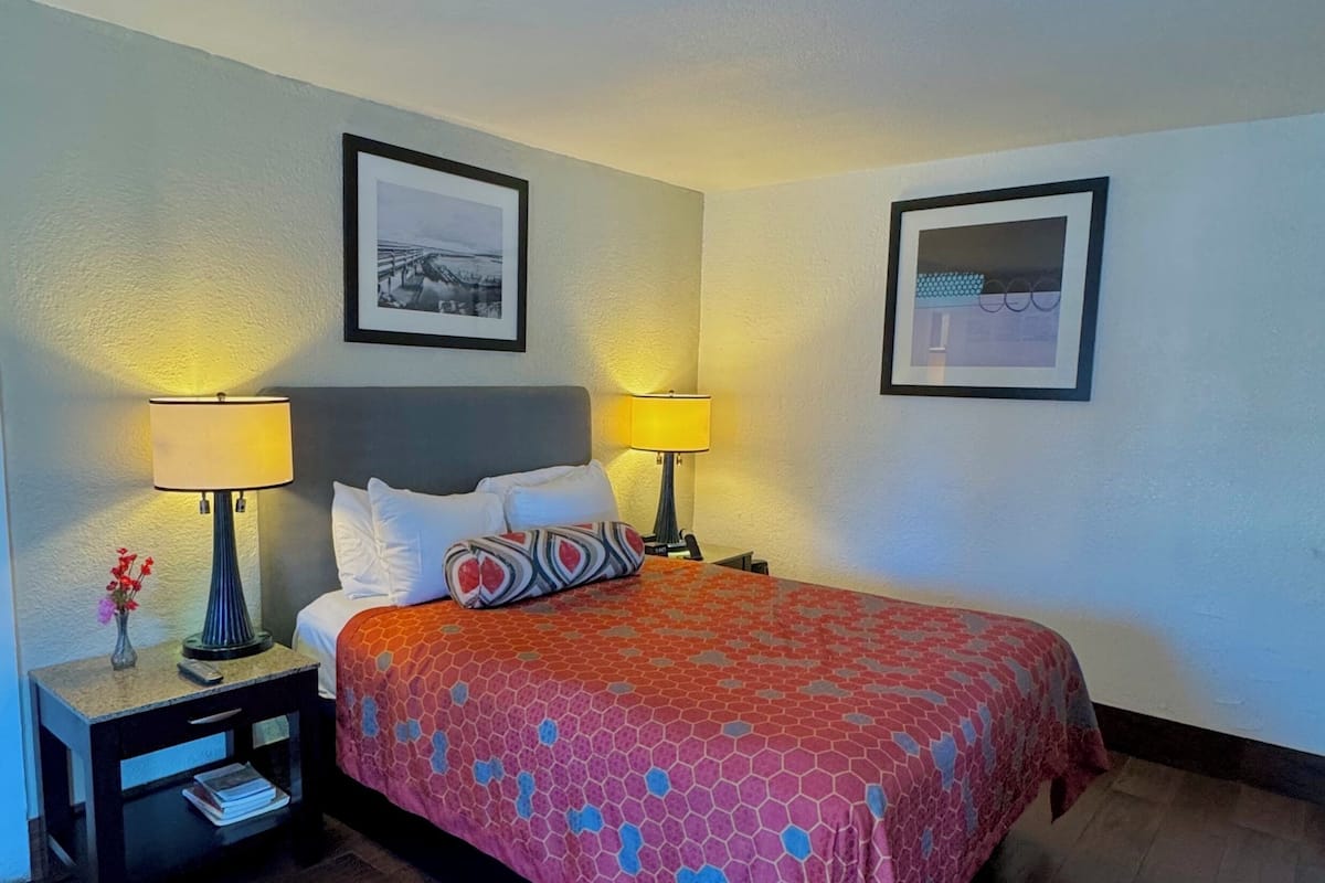 Une chambre d’hôtel avec un lit, deux tables de chevet, deux lampes et deux tableaux encadrés accrochés aux murs.