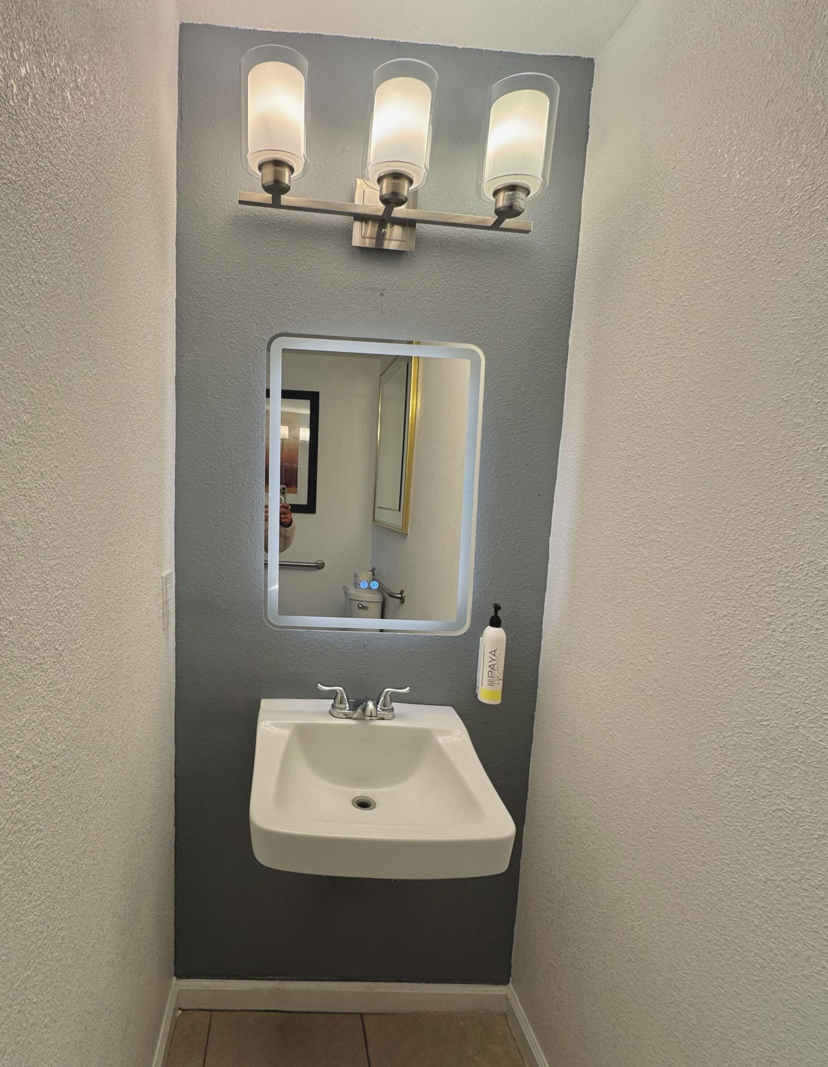 A bathroom with a white sink, a mirror, and three wall-mounted lights.