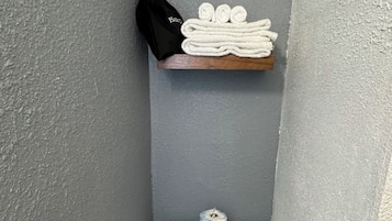 A small bathroom with a toilet, a towel rack with towels, a black bag, and a horse painting on the wall.