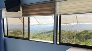 A room with a large window offering a view of a mountainous landscape. There is a table and a chair in the room. - Cabin2 of Height beautiful Panoramic view and Jacuzzi with hot water on terrace  (Provincia de Alajuela)