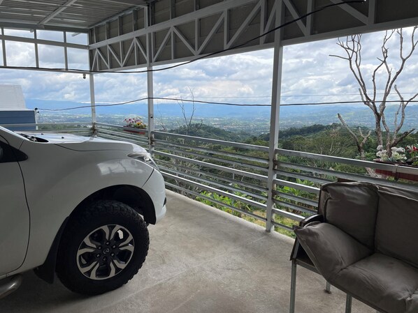 A white car parked inside a covered area with a view of a mountainous landscape.