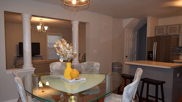 A modern dining area with a glass table surrounded by chairs, a kitchen with a refrigerator, and a hallway with a television. - Charming 4-bedroom house in welcoming Greenville with WiFi, AC (Greenville)