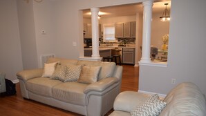 A living room with a beige sofa, a dining area with a kitchen in the background, and a large white column. - Charming 4-bedroom house in welcoming Greenville with WiFi, AC (Greenville)