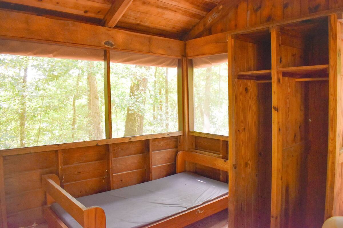 A small wooden cabin with a single bed, a window, and a shelf.