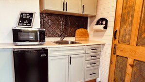 A compact kitchen with a dishwasher, a microwave, and a sink. There's a welcome sign, a wooden door, and a patterned rug. - NEWLY UPDATED Quiet Cottage Near Turkey Point and Port Dover (Simcoe)