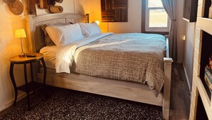 A bedroom with a bed, a nightstand, a lamp, a wall-mounted TV, and a window with curtains. - NEWLY UPDATED Quiet Cottage Near Turkey Point and Port Dover (Simcoe)