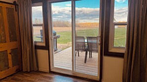 A room with a sliding glass door leading to an outdoor deck with chairs and a grill. - NEWLY UPDATED Quiet Cottage Near Turkey Point and Port Dover (Simcoe)