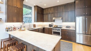 A modern kitchen with dark wood cabinets, a large island, stainless steel appliances, and a stone backsplash. - Telluride Sunset Ridge Home Spacious and Quiet! View of the Valley Floor and Wildlife (Telluride)