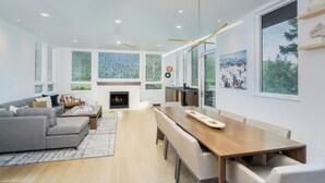 A modern living room with a fireplace, a dining area, and large windows offering a view of the outdoors. - Telluride Sunset Ridge Home Spacious and Quiet! View of the Valley Floor and Wildlife (Telluride)
