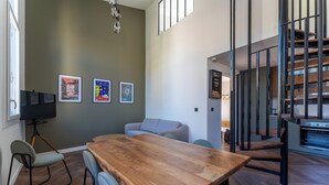 A modern living room with a wooden dining table, a sofa, and a staircase with a metal railing. - Duplex Bénézet - Welkeys (Avignon)