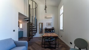 A modern living room with a blue sofa, a wooden dining table with chairs, a spiral staircase, and a view of a kitchen and dining area. - Duplex Bénézet - Welkeys (Avignon)