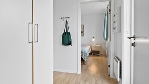 A hallway leading to a bedroom with a bed, bedside table, and a hanging bag.