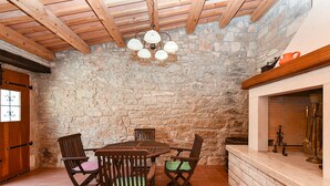 A rustic stone-walled room with a wooden ceiling, a stone fireplace, and a dining table with chairs.