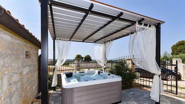 A hot tub under a pergola with a stone wall backdrop.